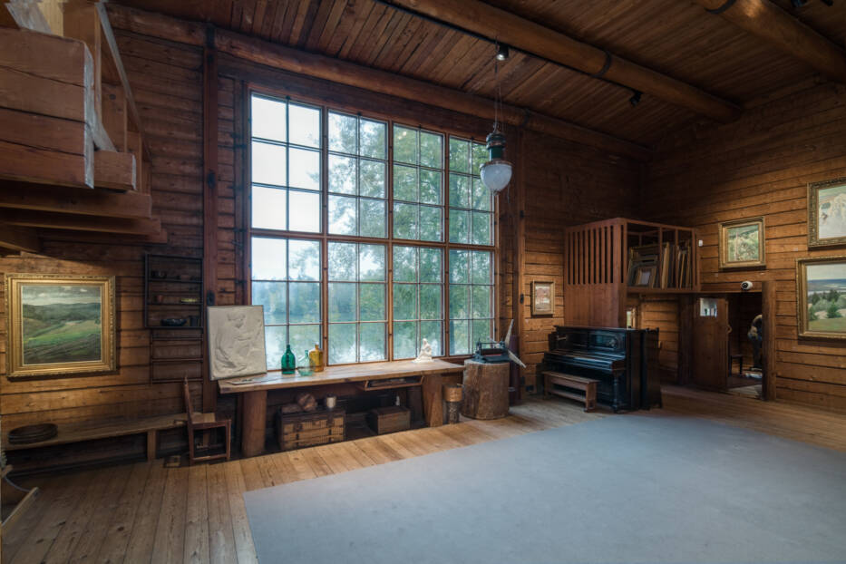Interior of Halosenniemi studio with wooden walls, large window, fireplace, and artist’s work area.